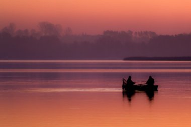 Silhouette of a fisherman catching fish in the boat at sunset clipart