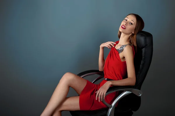 Sexy meisje in een rode jurk zittend in lederen stoel — Stockfoto