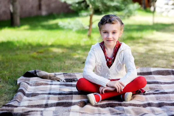 Child girl sitting on plaid in a garden — Stock Photo, Image