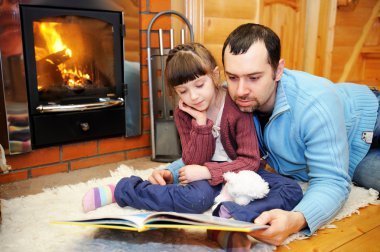 Father and daughter reading in front of fireplace clipart