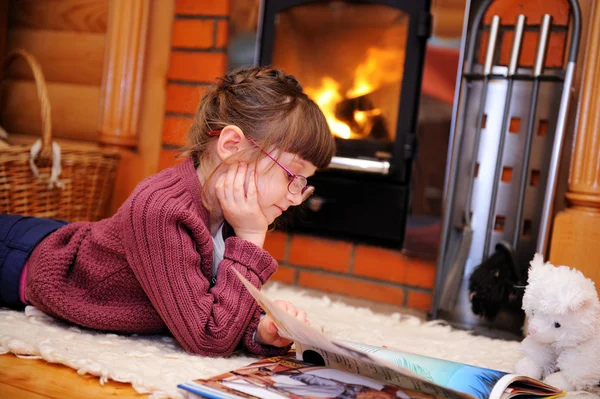 stock image Child girl is reading in front of fireplace