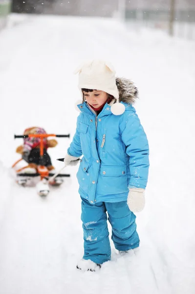 Little girl is pulling her snow scooter with a toy — Stock Photo, Image