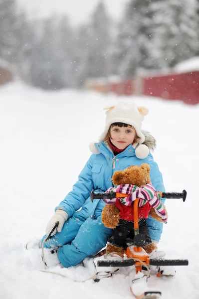 Little girl is riding her snow scooter with a toy — Stock Photo, Image