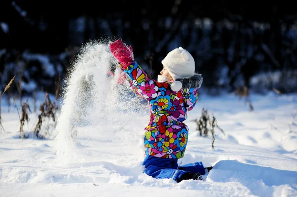 Toddler girl in colorful snowsuit plays in snow — Stock Photo, Image