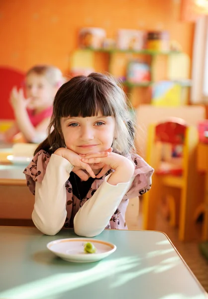 Happy little girl sitting at a table — Stock Photo, Image