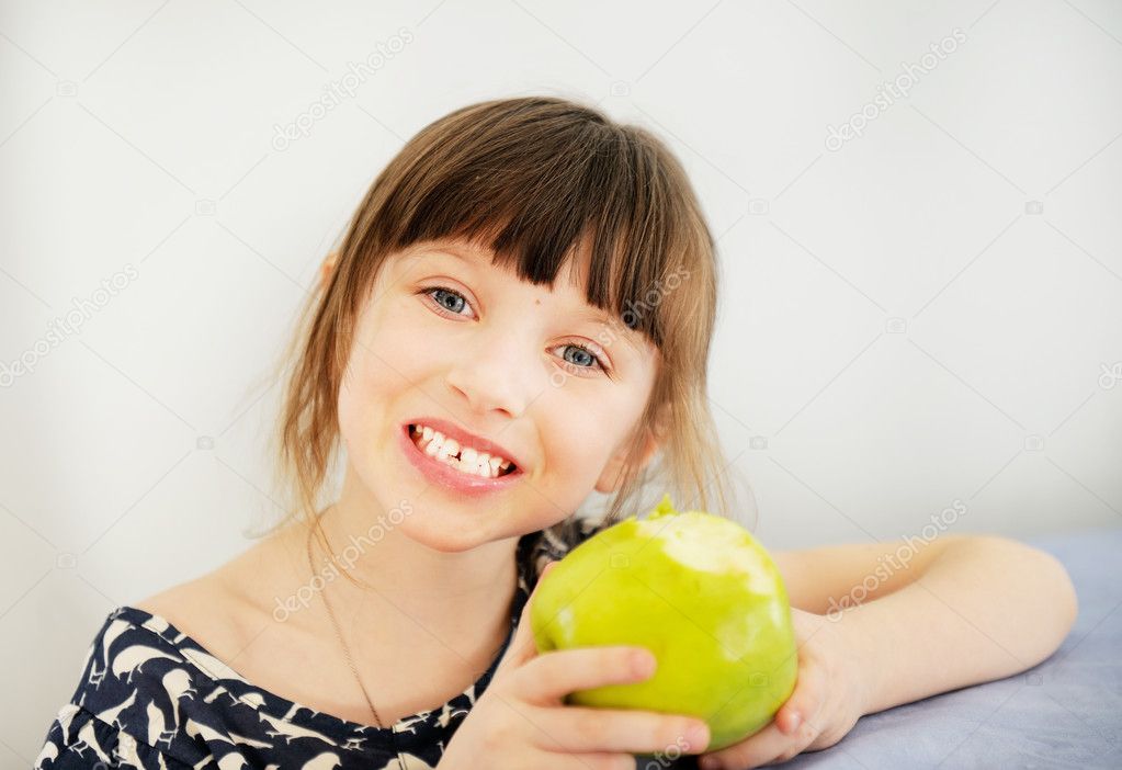 Happy child girl eating apple at home