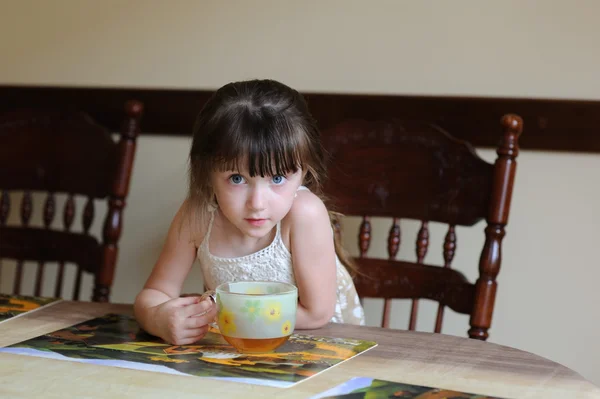 Маленькая девочка пьет чай в помещении за столом — стоковое фото