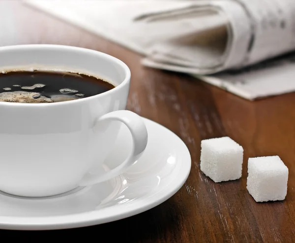 stock image Coffee cup, lump sugar and newspapers on a table