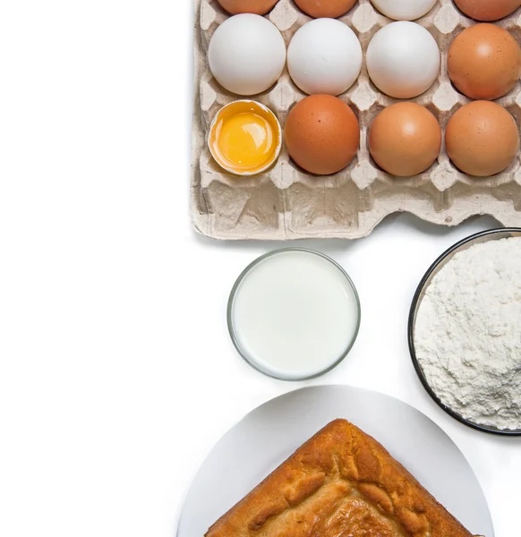 Raw eggs, glass of milk, flour and baked good — Stock Photo, Image