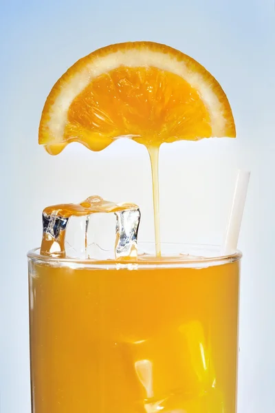 O suco de laranja está fluindo em um copo com gelo — Fotografia de Stock