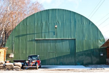 Old green aircraft hanger with classic car park in front clipart