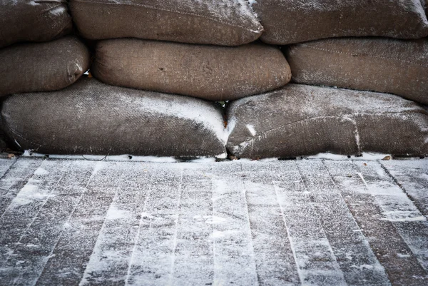 Velhos sacos de areia marrom na neve coberto piso de madeira — Fotografia de Stock