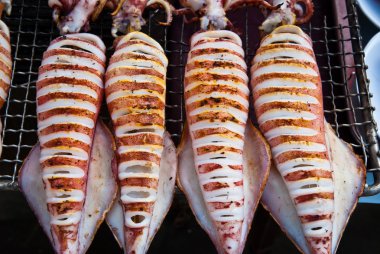 Flame grilled large squids on a bbq platform clipart