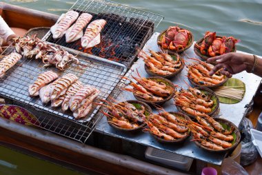 Thai traditional water market boat selling fresh squids and praw clipart