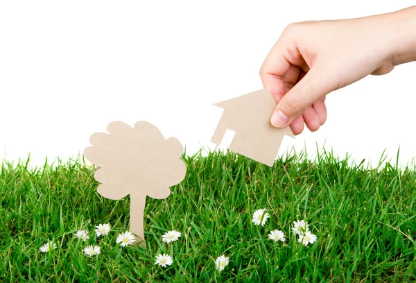 Mão mantenha o corte de papel da casa sobre a grama verde fresca da primavera — Fotografia de Stock