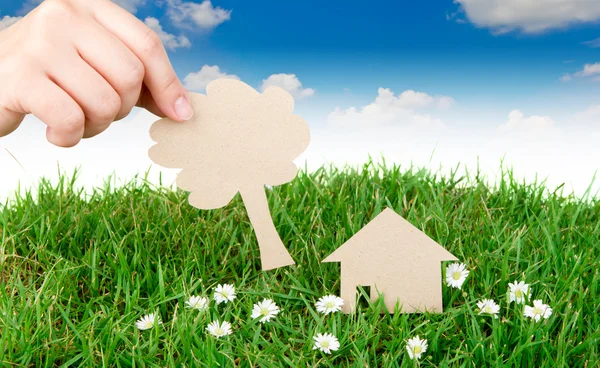 Ręka trzymać cięcia papieru domu nad trawa wiosna świeży zielony — Zdjęcie stockowe