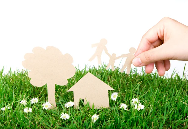 Ruka drží papír řez rodiny nad čerstvou jarní zelené trávy — Stock fotografie