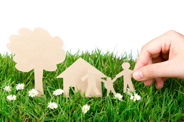 Ruka drží papír řez rodiny nad čerstvou jarní zelené trávy — Stock fotografie