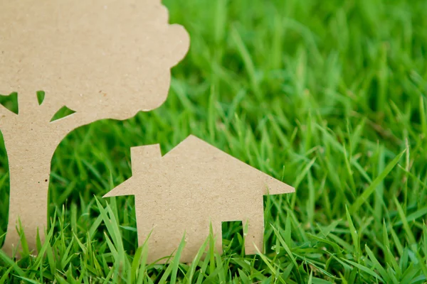 Papír řez domu a strom na svěží jarní zelené trávě — Stock fotografie