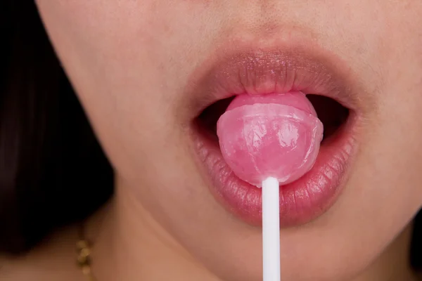 Woman licking a pink shiny lollipop on white background. — Stock Photo, Image