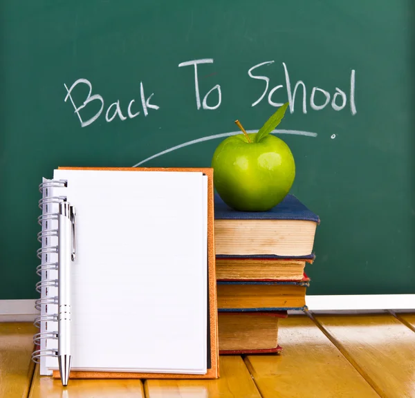 Tillbaka till skolan som skrivit på svarta tavlan med grönt äpple och böcker — Stockfoto
