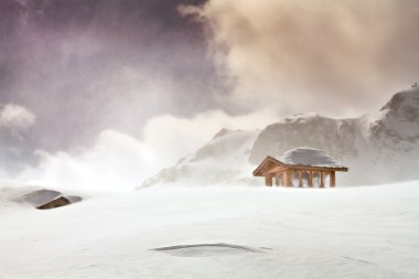 Wooden cottage and snow covered huts in blizard at the peak of s clipart