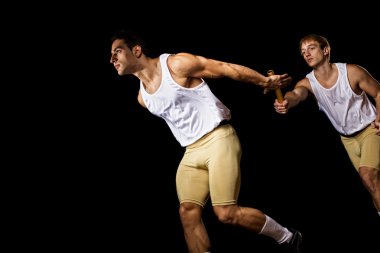 Relay racers passing the baton. Studio shot over black. clipart