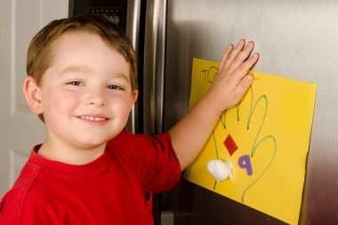 Child putting his art up on family refrigerator at home clipart