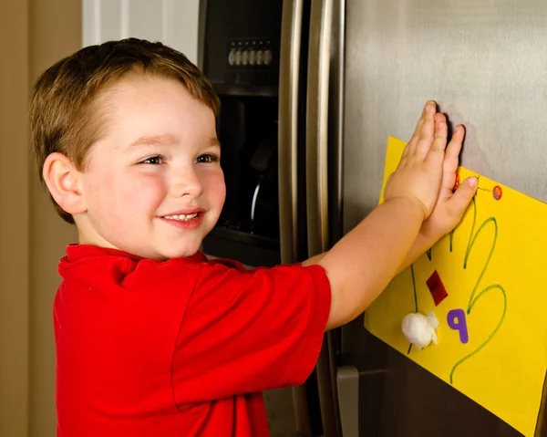 Barnet att hans konst sätta upp familjen kylskåp hemma — Stockfoto