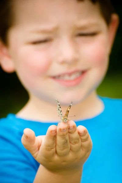Concepto de primavera con un primer plano de una mariposa dama pintada, Vanessa cardui, siendo sostenida por un niño jugando al aire libre en la naturaleza —  Fotos de Stock