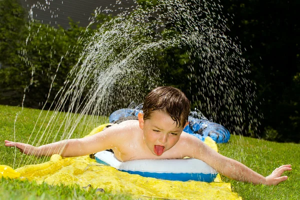 Niño feliz en el tobogán acuático para refrescarse en el día caliente durante la primavera o el verano —  Fotos de Stock
