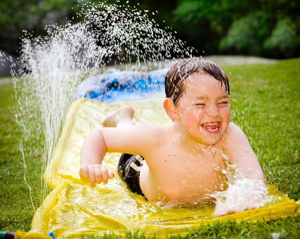 Bambino felice sullo scivolo d'acqua per rinfrescarsi nelle giornate calde durante la primavera o l'estate — Foto Stock