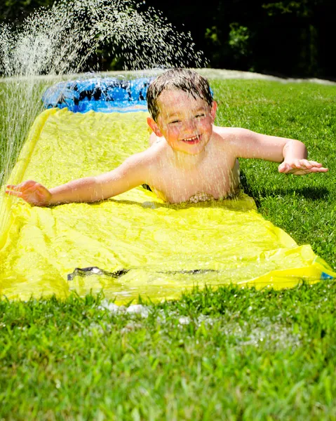 Happy child on water slide to cool off on hot day during spring or summer — Stockfoto