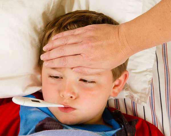 Sick child boy being checked for fever and illness while resting in bed — Stock Photo, Image