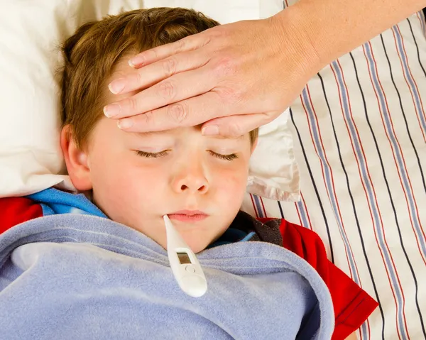 生病的孩子男孩正在发烧和病在床上休息的同时检查 免版税图库照片