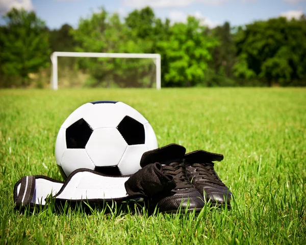 Child sports concept with soccer ball, cleats, shin guards on field with copy space — Stock Photo, Image