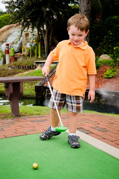 Niño juega mini golf en campo de putt putt —  Fotos de Stock