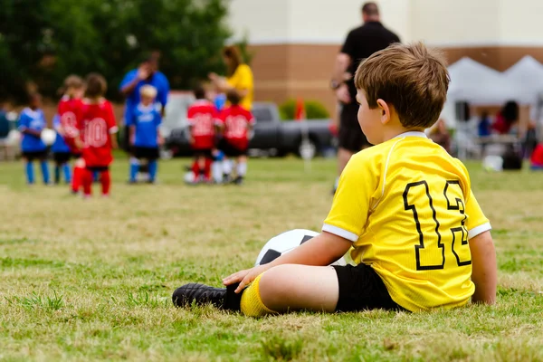 Menino criança de uniforme assistindo futebol juvenil organizado ou jogo de futebol de linhas laterais — Fotografia de Stock