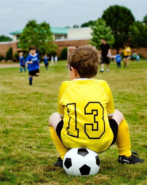 Niño pequeño en uniforme viendo fútbol juvenil organizado o partido de fútbol desde un costado — Foto de Stock