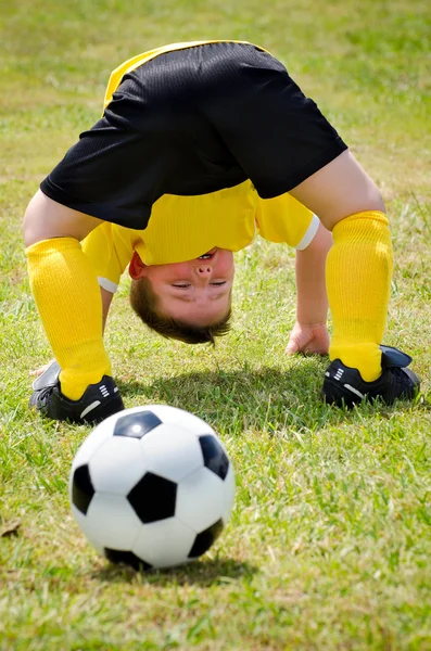 Jovem criança assiste bola de futebol passar por suas pernas durante o jogo organizado da juventude — Fotografia de Stock