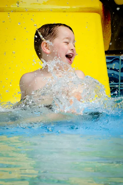 Giovane ragazzo o bambino si diverte spruzzando in piscina dopo essere sceso scivolo d'acqua durante l'estate — Foto Stock