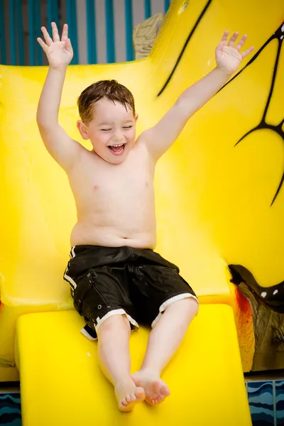 Fiatal fiú vagy gyerek szórakozás fröccsenő medencébe, miután lemegy a csúszda nyáron — Stock Fotó