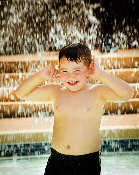 Criança brincando sob cachoeira na piscina — Fotografia de Stock