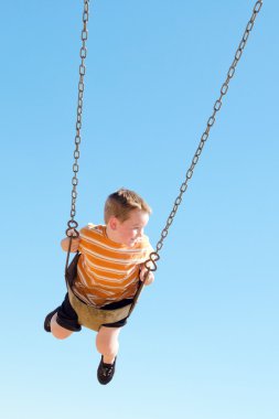 Cute young boy swings at kid park playground clipart