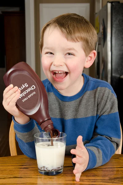 Young boy pouring sugar free syrup to make chocolate milk at dinner table — Stock Photo, Image