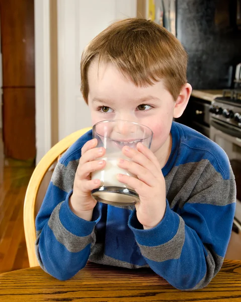 Young boy drinking milk at dinner table — Stock Photo, Image