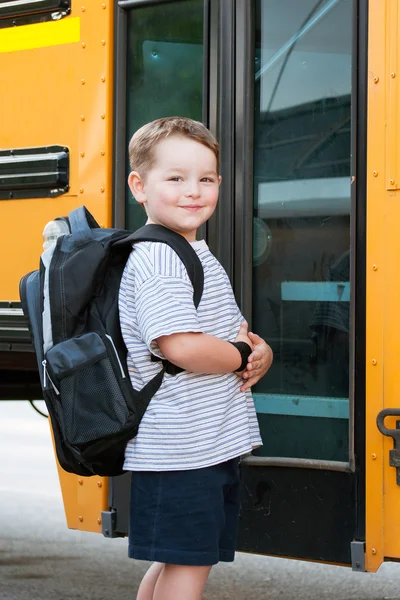 Happy young boy in front of school bus going back to school — Stock Photo, Image