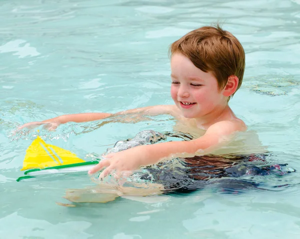 Ung pojke leker med leksak båt medan du svalkar av dig i poolen varm sommardag — Stockfoto