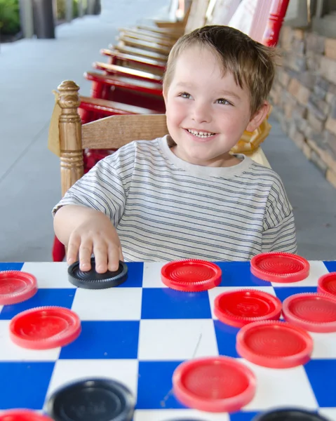 Smiling young boy playing checkers while sitting on rocking chair on porch — Stock Photo, Image