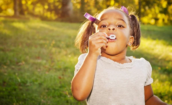 Unga afroamerikanska flicka som leker med bubblor i park — Stockfoto